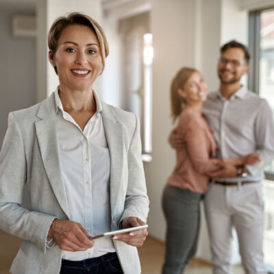 Portrait of happy real estate agent with a couple in the backgro